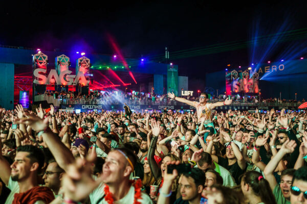 A lively crowd of festival-goers with hands raised enjoying a night concert with bright stage lights and 