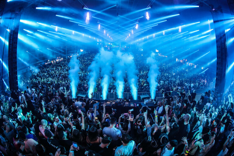 A vibrant concert scene with an energetic crowd and a stage with blue lights and smoke effects.