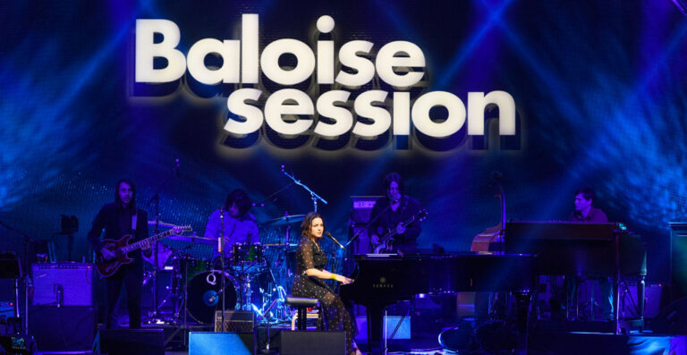 Band performing on stage with the words "Baloise Session" projected in large letters behind them.