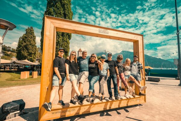 A group of eight people posing together inside a large wooden frame that reads 