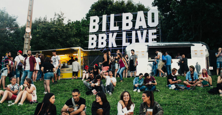 People socializing and enjoying themselves at an outdoor music festival with large "BILBAO BBK LIVE" letters in the background.