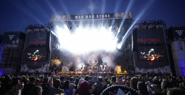A crowd of people at a music festival watching a live performance on a large stage named 