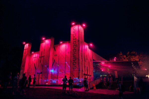An outdoor nighttime scene with a large building illuminated by red lighting and the word 