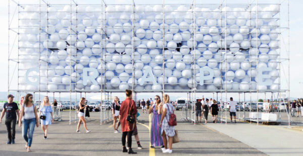 People walking near a large scaffolding structure adorned with numerous balloons and the letters 