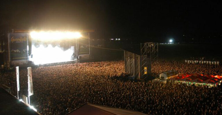 A massive crowd of people gathered at night for an outdoor concert, with bright stage lights illuminating the event.