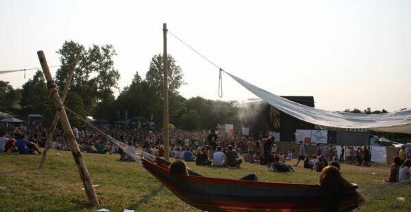 Outdoor festival scene with people sitting on the grass, a stage in the background, and a hammock in the foreground.