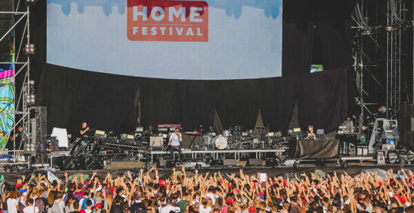 A crowd of festival-goers with raised hands in front of a stage with musicians and equipment at the 