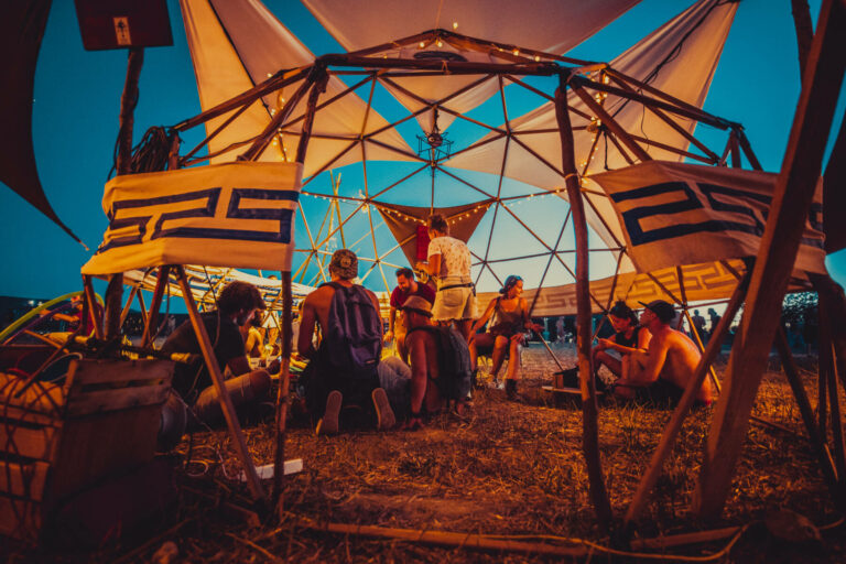 Group of people sitting and socializing under a geodesic dome tent with string lights at dusk.
