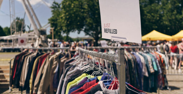 A clothing rack filled with various garments at an outdoor market with a sign stating 