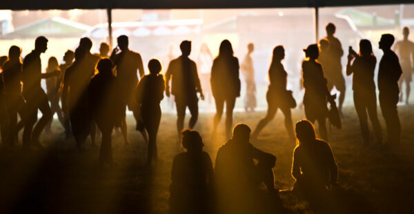 Silhouetted people at an outdoor event during dusk, with a warm light creating a glow and shadows around the figures.