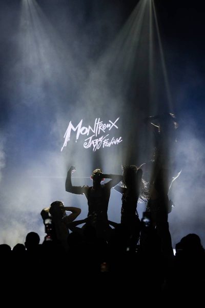 Silhouettes of performers on stage with dramatic lighting at the Montreux Jazz Festival, as seen by an audience.