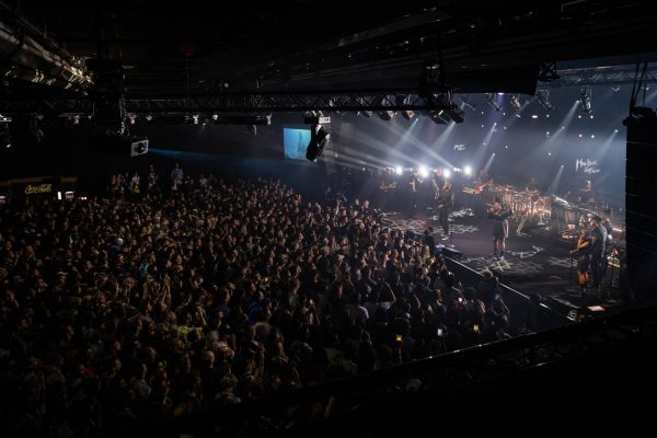 A crowded concert hall with Stormzy performing on stage, spotlights shining, and a large audience watching and enjoying the performance.