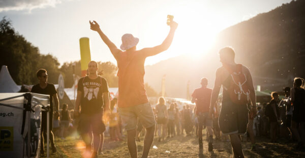 People enjoying a music festival during a sunny sunset, with one person in the foreground raising his arm victoriously.