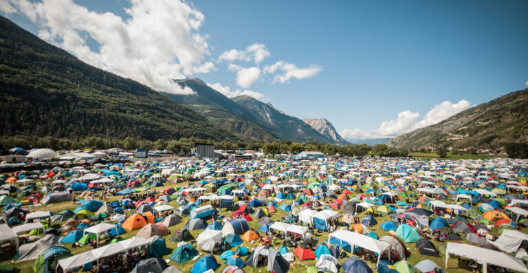 A vast array of colorful tents packed closely together at a festival in a valley with mountains in the background and a clear blue sky overhead.
