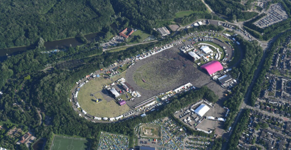 Aerial view of an outdoor music festival with large crowds, stages, and surrounding green areas.
