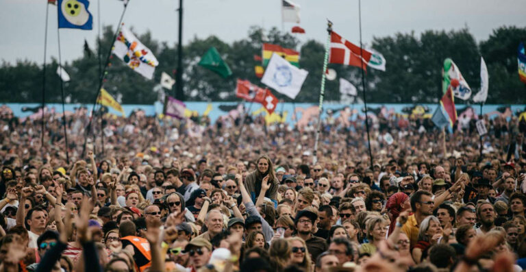 A large crowd at an outdoor festival with several people holding up flags, one person standing out in the crowd raised on someone's shoulders.