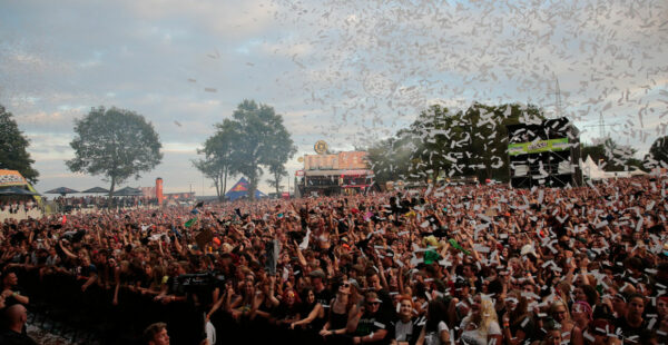 A large crowd at an outdoor music festival with confetti falling from the sky.