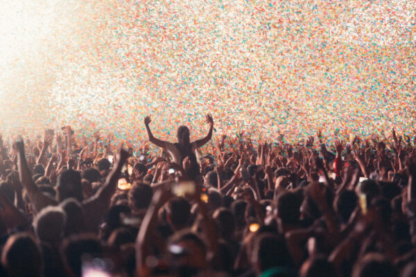 A crowd of people at a concert with their hands raised, enjoying a confetti explosion.