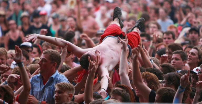A shirtless man is crowd surfing over a large group of concert-goers.