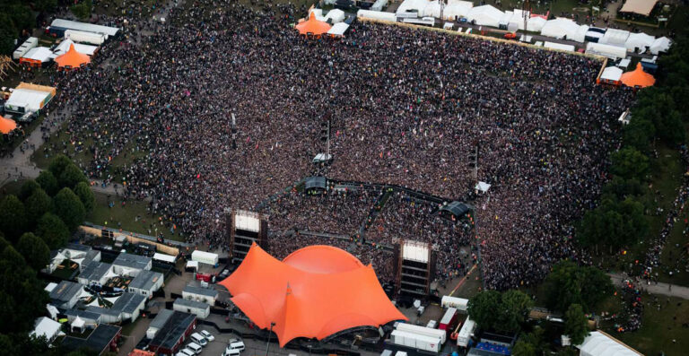 Aerial view of a densely crowded outdoor music festival with multiple stages and vendor tents.