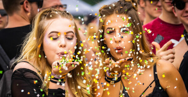Two women at a festival blowing colorful confetti from their hands.