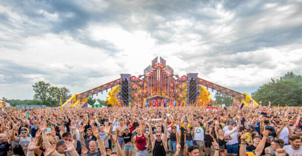 A large crowd of festival-goers cheering in front of a grand stage with elaborate lighting and design during the daytime.