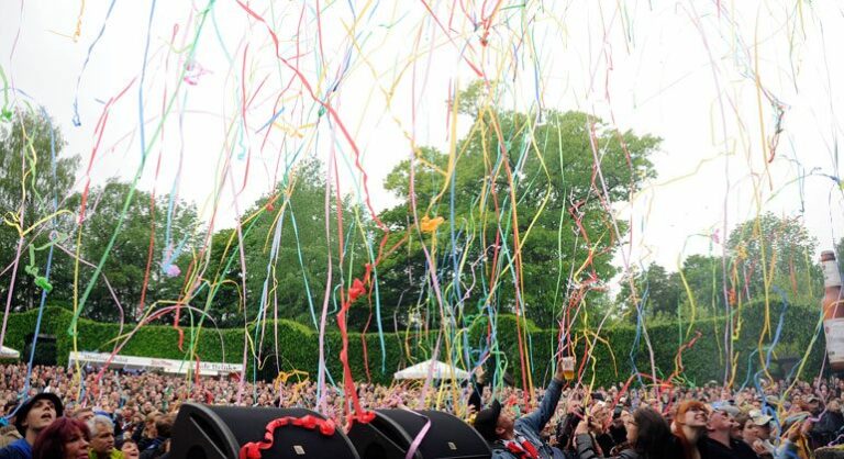 A crowd of people at an outdoor event with colorful streamers flying through the air.
