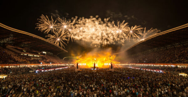 Fireworks illuminating the night sky above a crowded stadium during a live event.