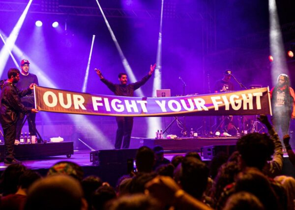 People on stage at a concert holding a banner that reads 