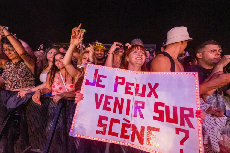 A crowd of excited people at a concert with one person holding up a large sign that reads 