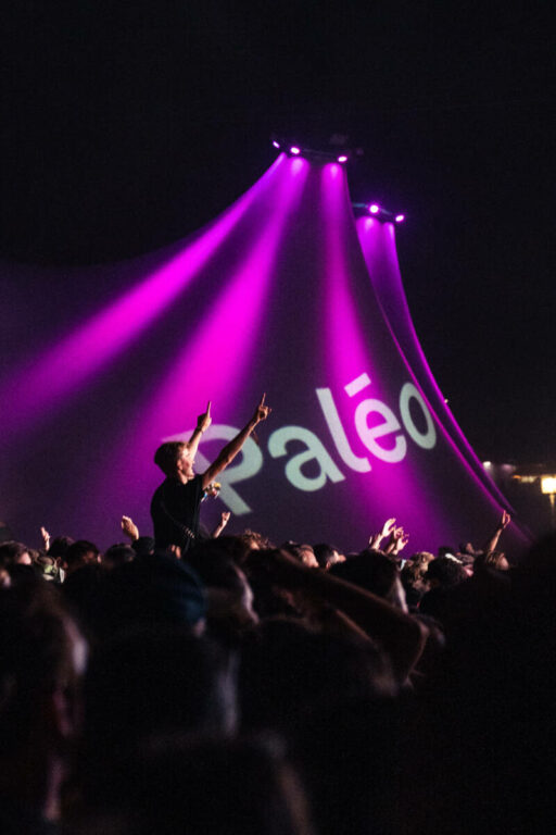 Crowd of people at a concert with purple stage lights and the word 