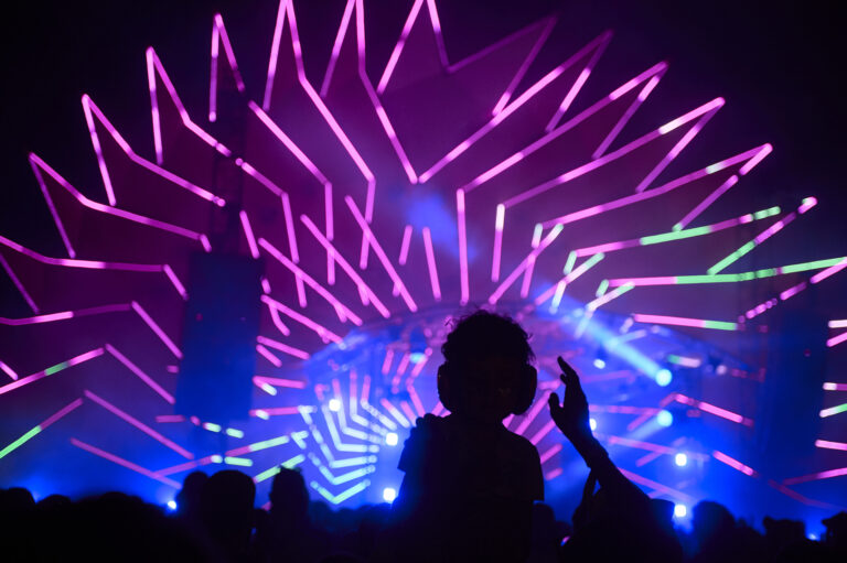 A silhouette of a person at a concert with vibrant neon purple and blue illumination forming a starburst pattern on stage.
