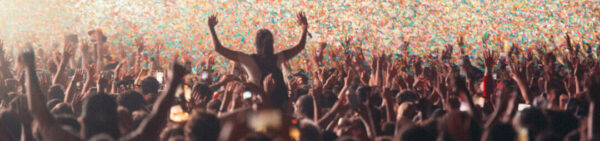 A crowd of people at a concert with their hands up, some in silhouette, under a shower of colorful confetti.