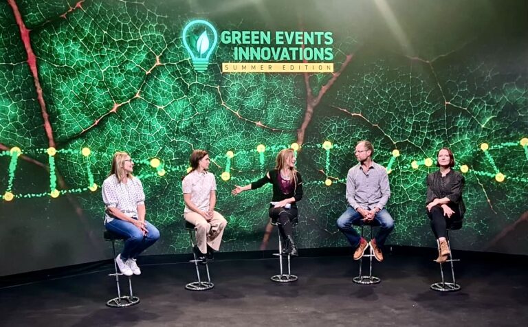 Five people seated on stools participating in a panel discussion against a backdrop with a green leaf pattern and the words 
