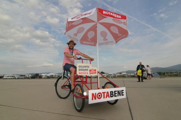 A person riding a promotional tricycle with a red and white canopy labeled 