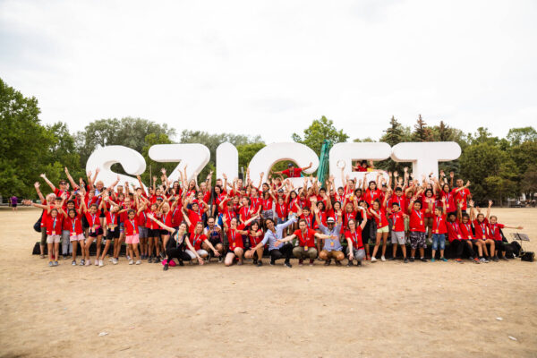 A large group of cheerful people, many wearing red shirts, posing for a photo in front of oversized white letters spelling 