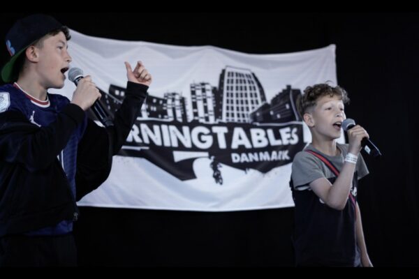 Two young boys holding microphones and performing on stage in front of a banner that reads 