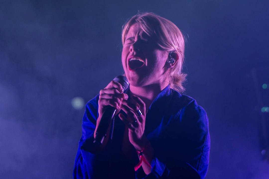 Female singer passionately performing on stage with a microphone, emotional expression, illuminated by purple stage lights.