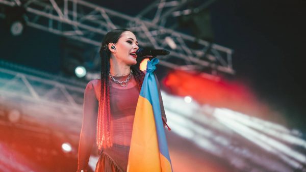 Singer performing on stage, holding a microphone with a Ukrainian flag tied to it.