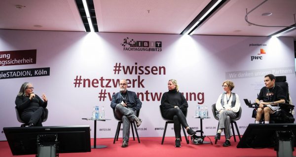Panel discussion taking place at IBIT Fachtagung 2023, with five participants sitting on a stage in front of a backdrop with hashtags.