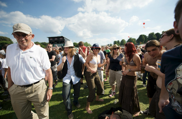 A group of people enjoying an outdoor festival on a sunny day, with some dancing and others watching.