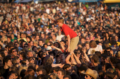 A large crowd at an outdoor music festival with a man crowd surfing near the center.