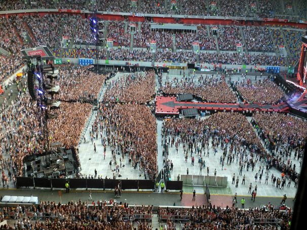 A large concert audience in a stadium with a central stage and extended catwalks.