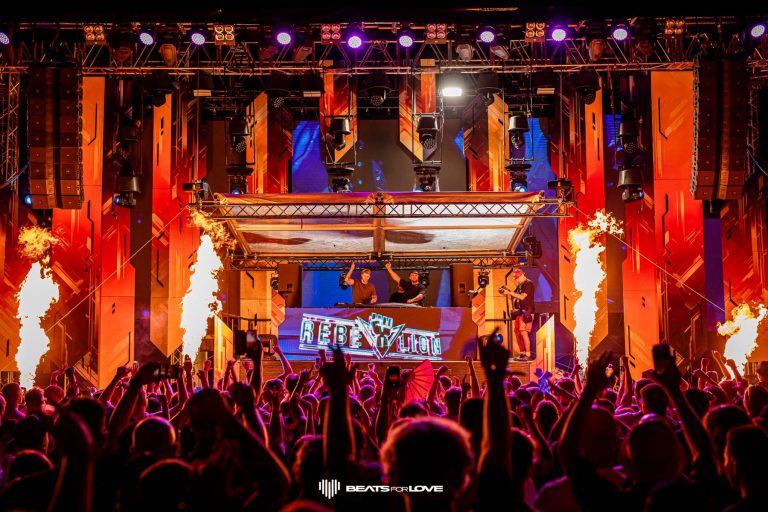 Crowd at a lively electronic music festival with DJs performing on a stage labeled 