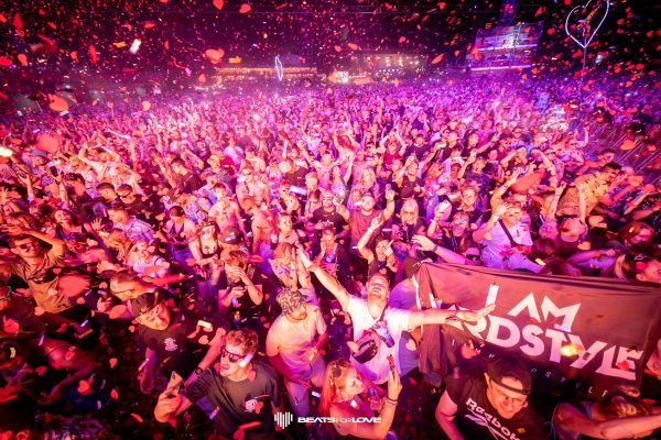 Crowd of people dancing and celebrating at a nighttime music festival with red confetti falling and a 