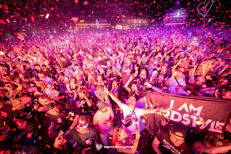 Crowd of people dancing and celebrating at a nighttime music festival with red confetti falling and a 