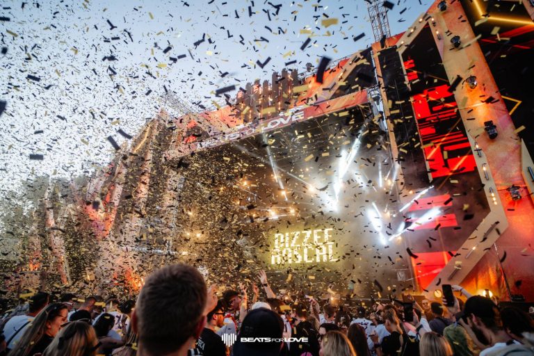 Crowd enjoying a music festival with confetti falling in front of a stage displaying 