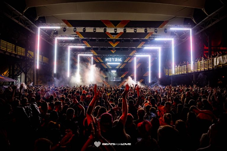 Large crowd at an indoor music concert with light installation framing the stage and 