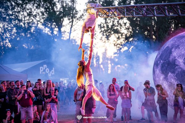 Two acrobats performing a balancing act at an outdoor event with a crowd watching in the background.