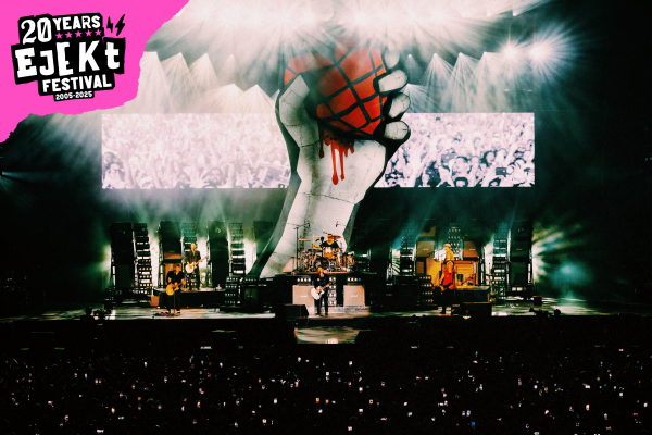 Rock band performing on stage with a large backdrop of a hand gripping a bleeding basketball at Ejekt Festival's 20th anniversary event.